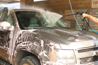 Spray nozzle rinsing soap off the windshield of a vehicle.